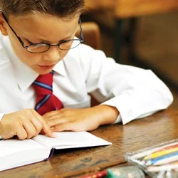Small boy in a white shirt and red tie reading from a book.