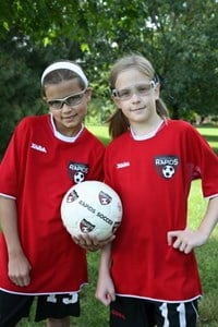 Two young girls in red jerseys holding a soccer ball.